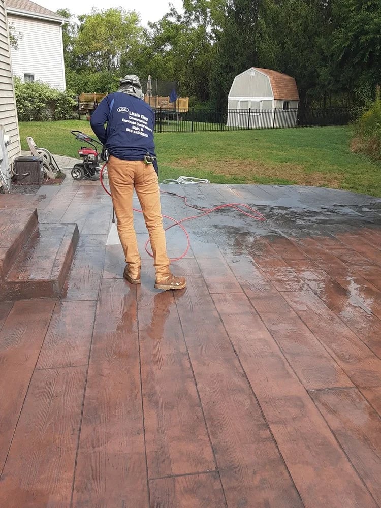 Worker pressure washing a wet wooden deck in a residential backyard during daytime