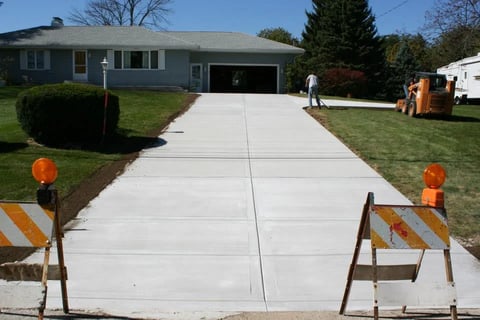 New concrete driveway with caution barriers and orange markers in front of single-story house