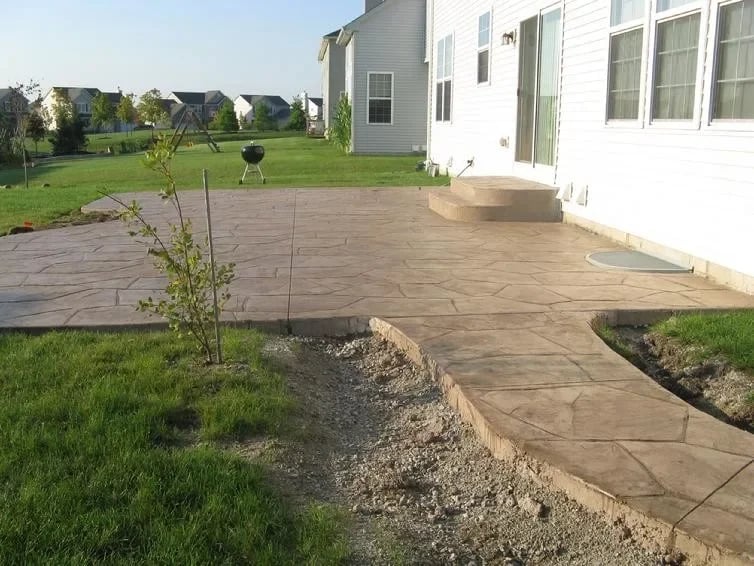 New concrete patio attached to white house with green lawn and landscaping
