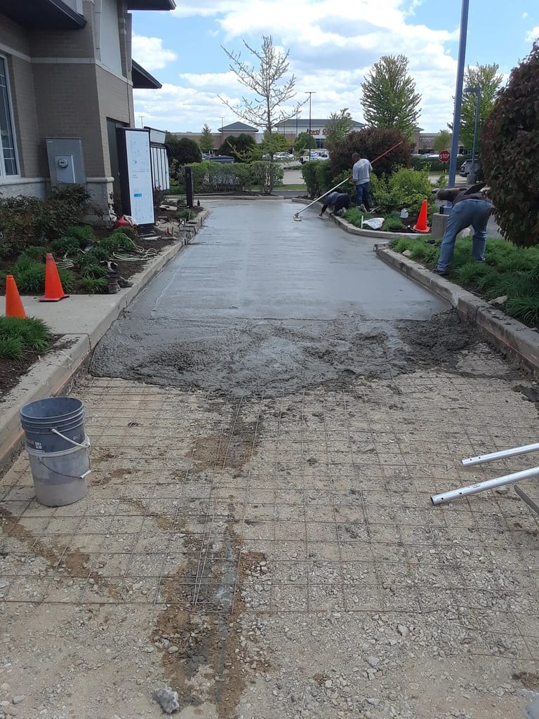 Construction workers pouring concrete on residential driveway with orange safety cones and tools visible