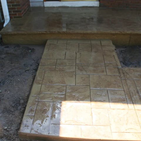 Tiled concrete patio with geometric pattern laid out in front of a brick building foundation