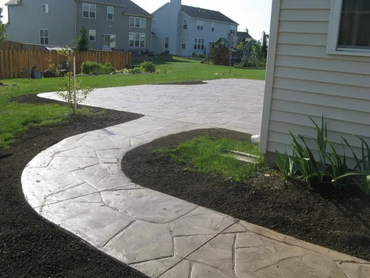 Curved stamped concrete patio pathway in residential backyard with landscaping and homes in background