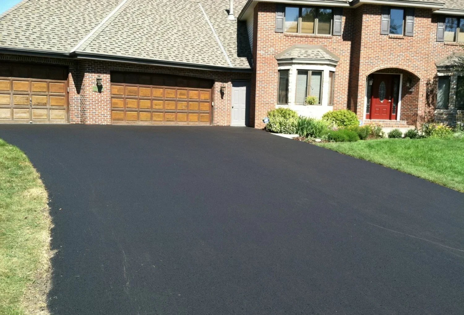 Newly paved black asphalt driveway leading to a brick home with two-car garage and red front door